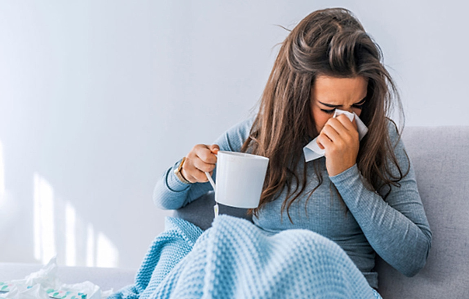 Immunsystem stärken: Erkältete Frau sitzt auf Couch mit einer Tasse Tee